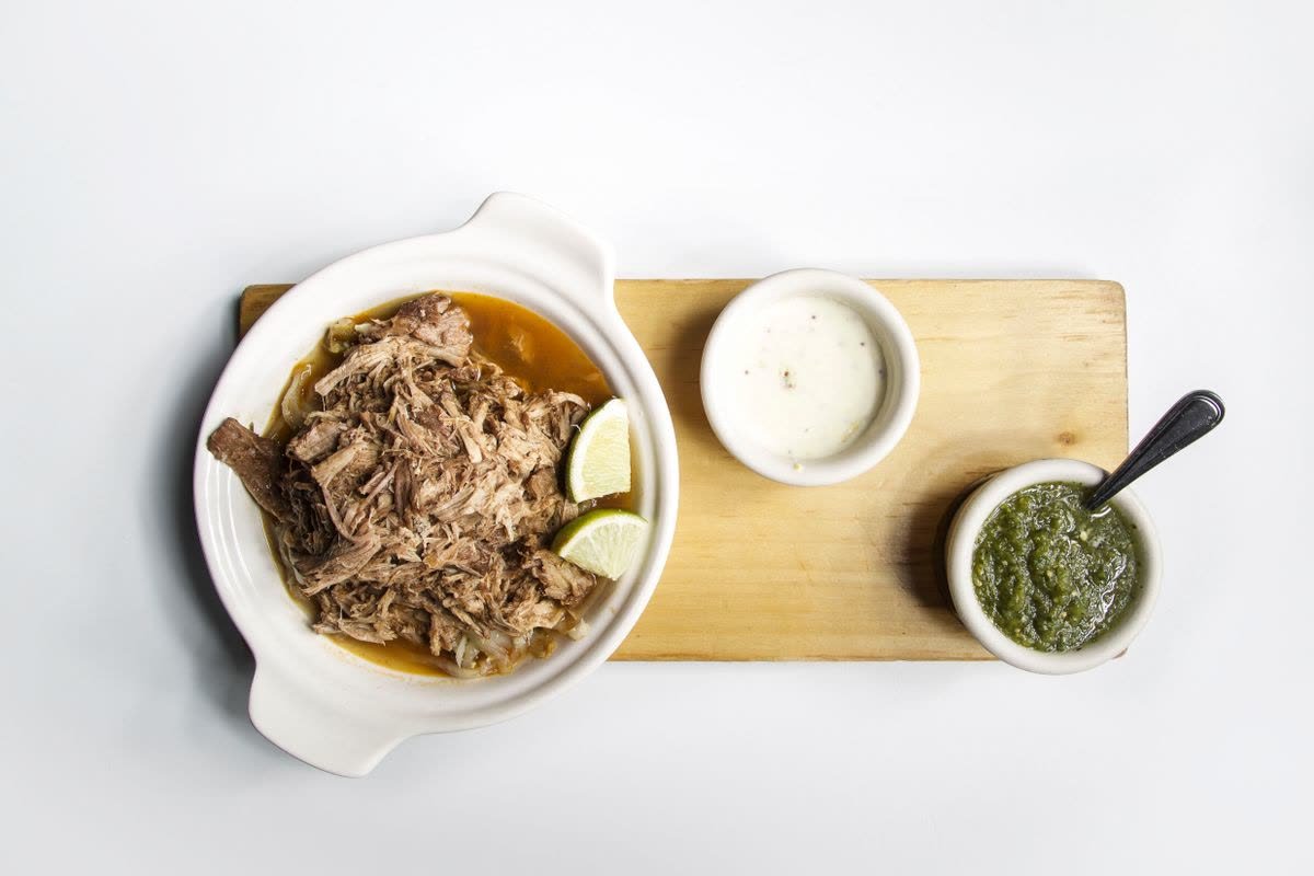Sönderdraget nötkött i en vit gryta, serverat med lime och två såser.