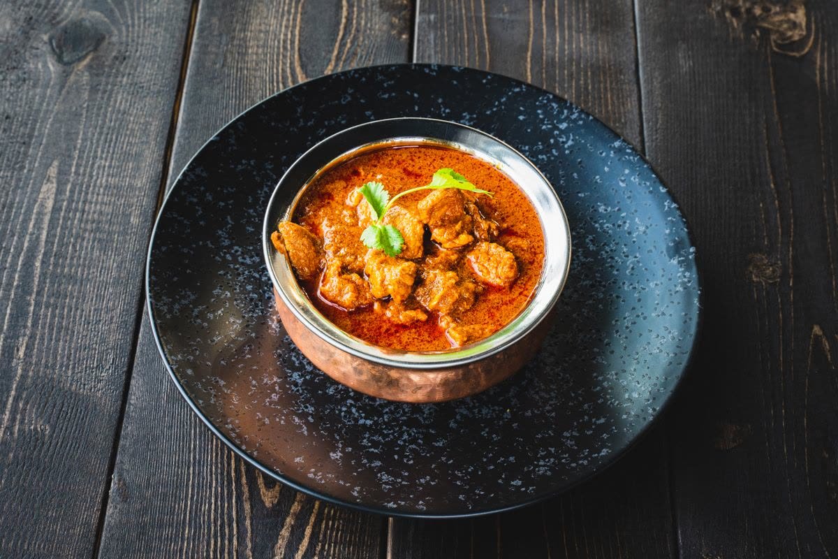 Kyckling tikka masala i röd currysås serverad i en kopparskål.