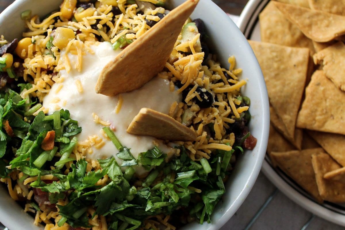 Vegetarisk chili med bönor, riven ost, gräddfil och koriander, serverad med nachochips.